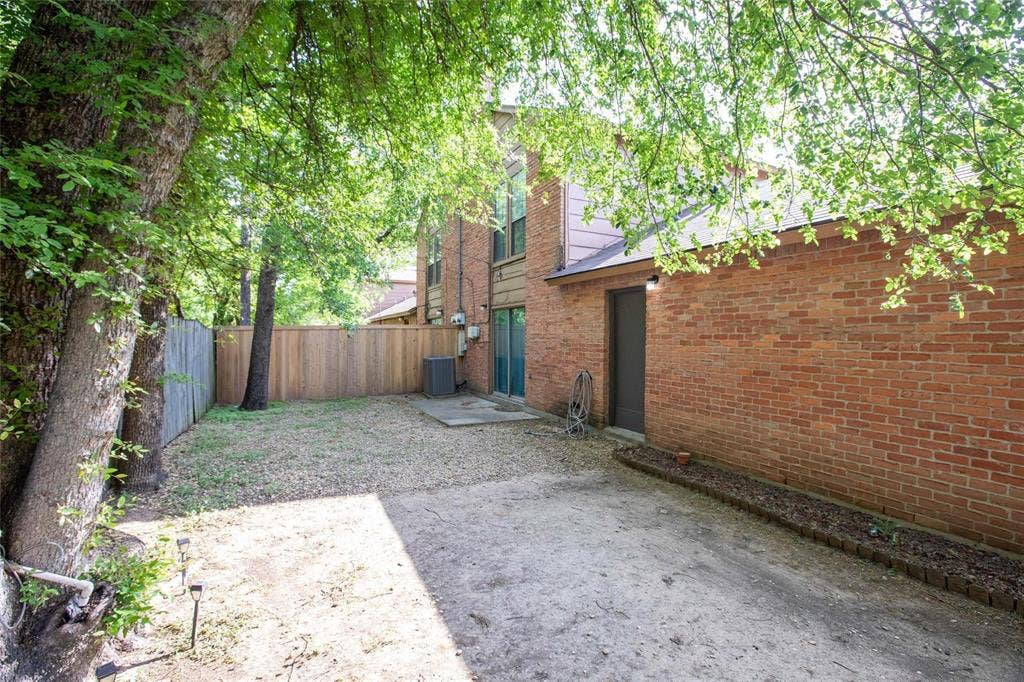 Exterior red brick facade featuring a wood privacy fence, concrete patio, and mature trees