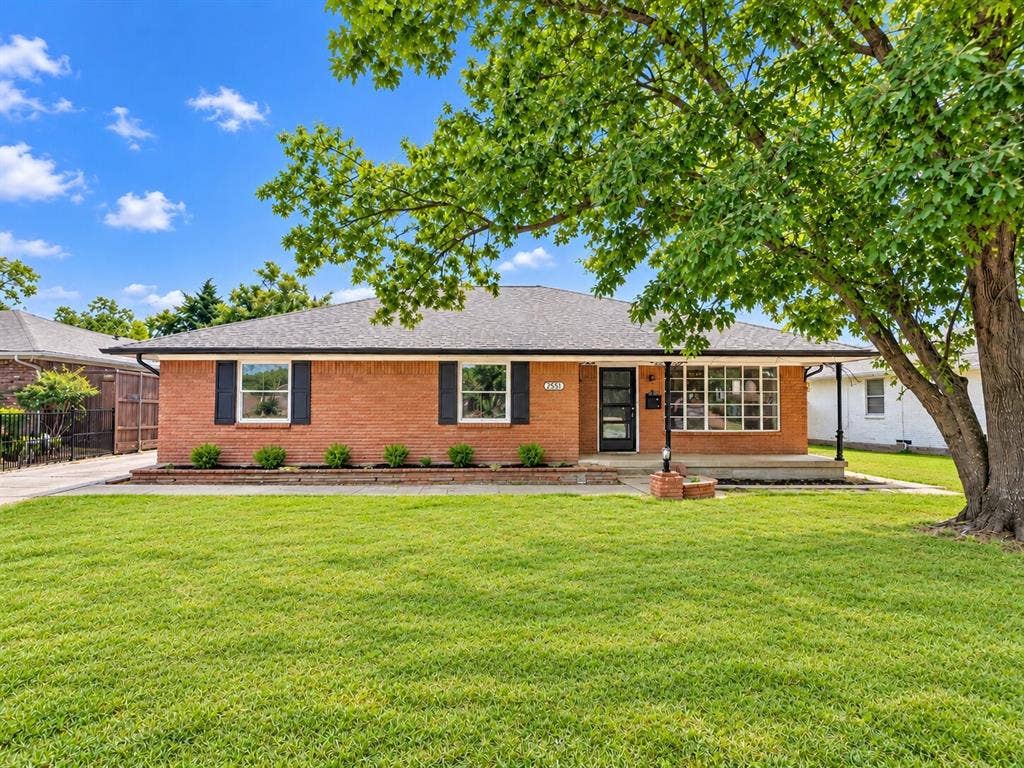 2551 Pinebluff Drive, Dallas, TX 75228 Single-story brick exterior featuring a hip roof, expansive front lawn, shuttered windows, and a covered porch with a brick-surround support pillar