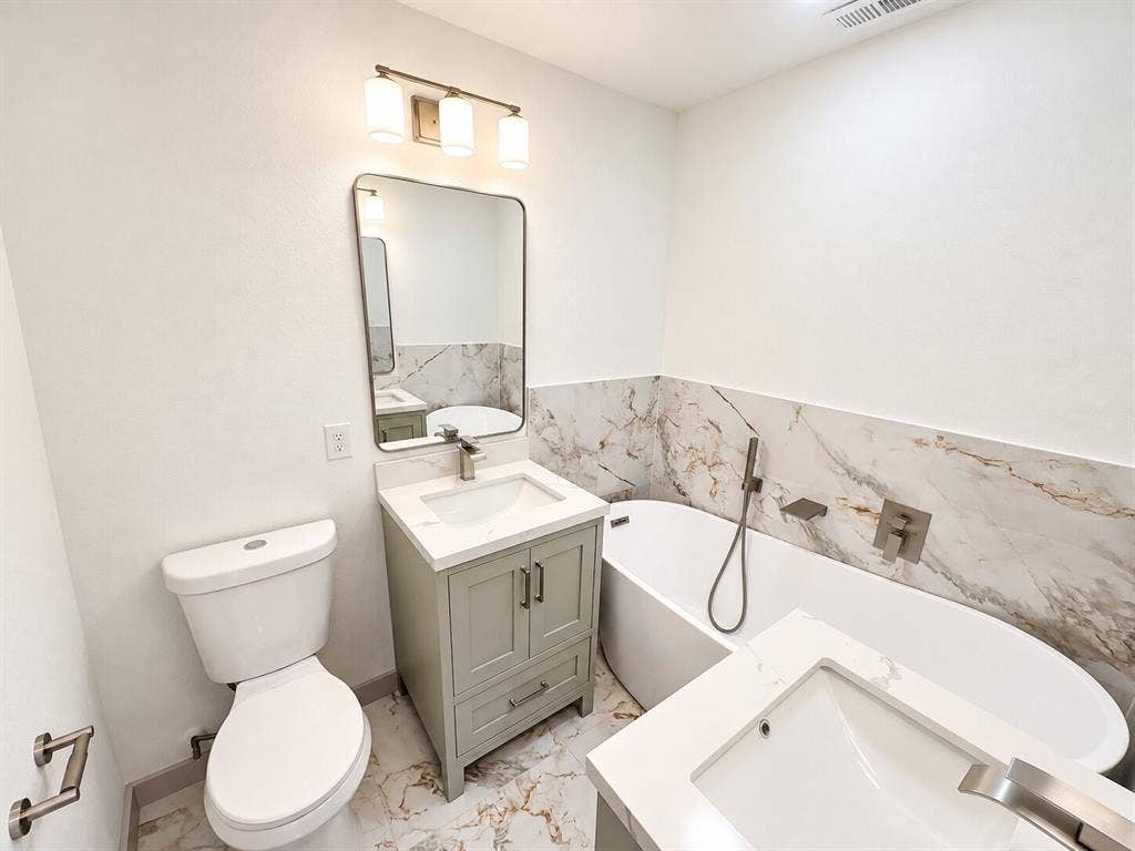 2551 Pinebluff Drive, Dallas, TX 75228 Bathroom featuring a freestanding soaking tub, stone-patterned wall tile, dual vanities with quartz countertops, undermount sinks, and a brushed nickel finish faucet set
