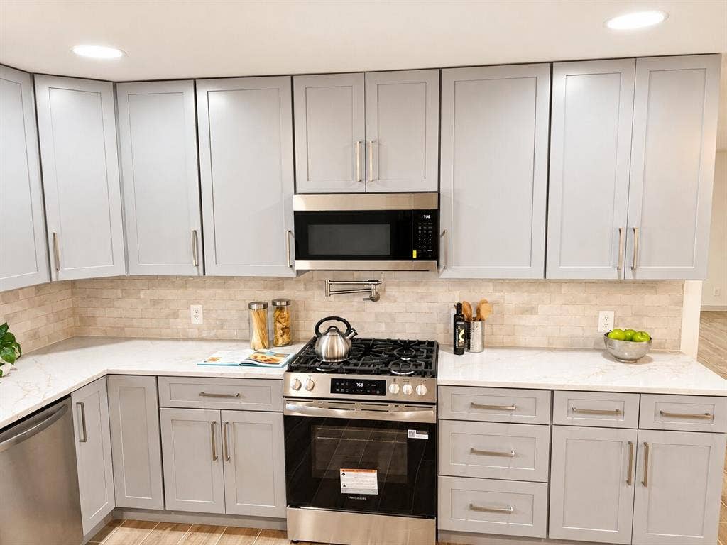 2551 Pinebluff Drive, Dallas, TX 75228 Kitchen featuring light gray Shaker-style cabinetry, white stone-finish countertops, stainless steel appliances, a built-in over-the-range microwave, and a textured stone tile backsplash with a wall-mounted pot filler