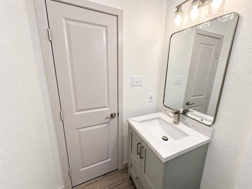 2551 Pinebluff Drive, Dallas, TX 75228 Bathroom featuring a sage green vanity with white stone-finish countertop, integrated rectangular sink, wall-mounted metallic faucet, rounded-corner mirror, and three-light fixture