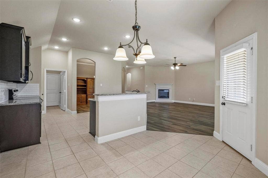 Open-concept interior featuring wood-finish flooring, a stone-surround fireplace, a peninsula with stone countertop, recessed lighting, and a multi-arm chandelier