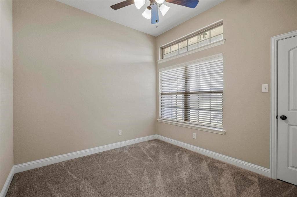 Neutral-toned interior room featuring carpeted flooring, a ceiling fan with integrated lighting, and a large window topped with a rectangular transom