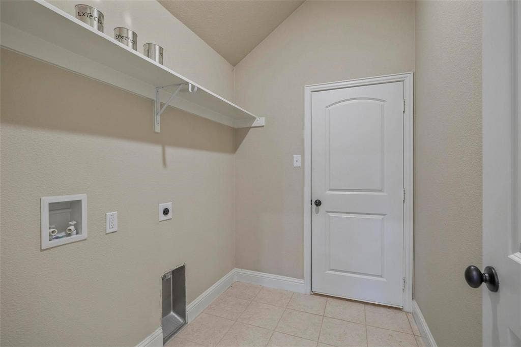 Utility area featuring tile flooring, vaulted ceiling, built-in wall shelving, and a single-panel arch-top interior door