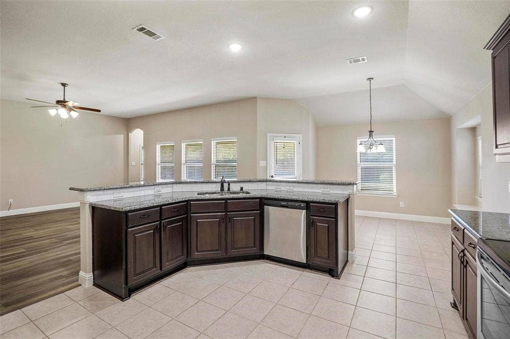 Kitchen featuring dark cabinetry, stone-finish countertops, stainless steel dishwasher, tile flooring, and vaulted ceilings