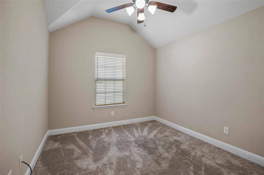 Room featuring a vaulted ceiling, neutral wall tones, neutral carpeting, and a ceiling fan with integrated lighting