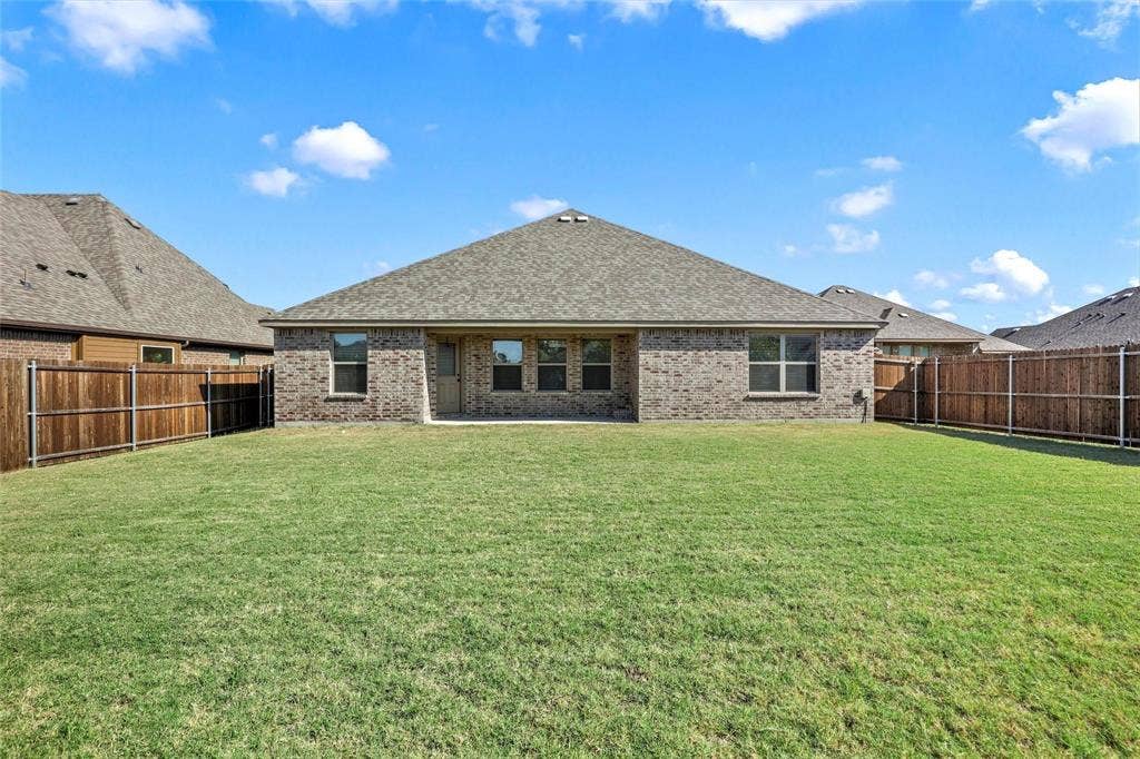 Brick exterior finish, hipped roof, multi-pane windows, and fenced backyard with grass lawn