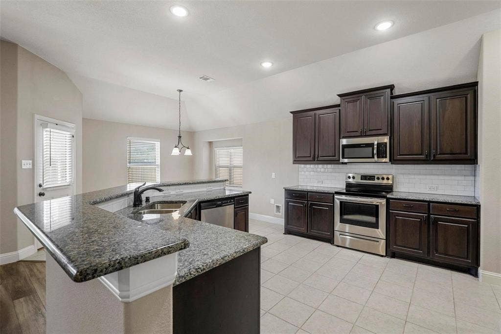 Kitchen featuring dark wood cabinetry, stone-finish countertops, stainless steel appliances, subway tile backsplash, and vaulted ceilings