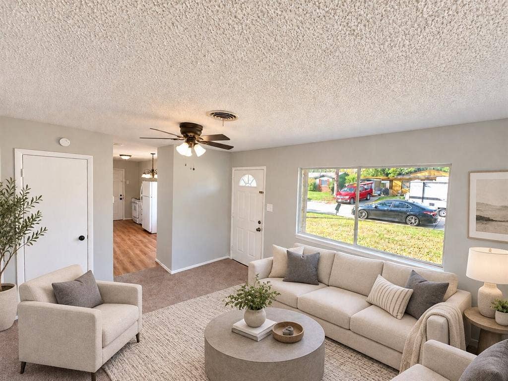 Interior space featuring neutral-toned wall paint, a large single-pane window, carpeted flooring, and a ceiling-mounted fan with integrated lighting
