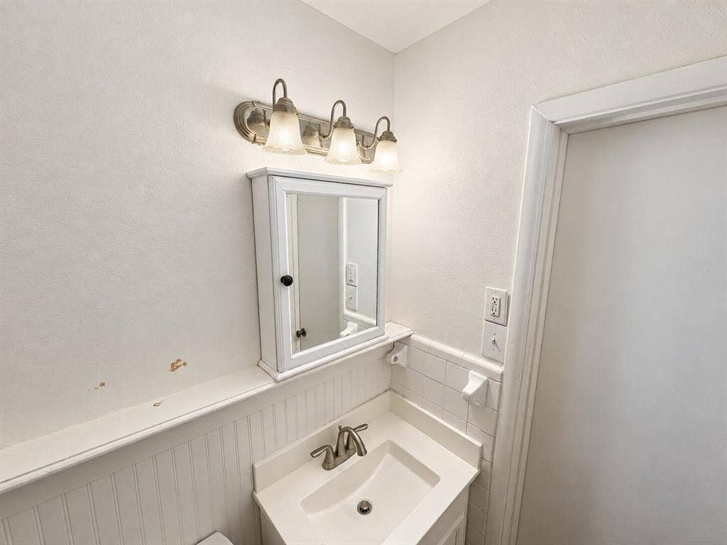 Wall-mounted medicine cabinet, integrated basin vanity, beadboard wainscoting, and three-light brushed-finish vanity fixture