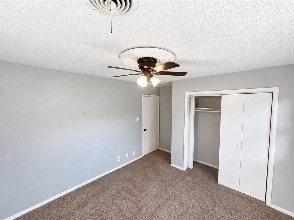 Neutral-toned room featuring wall-to-wall carpeting, a central ceiling fan with an integrated light fixture, and a white bifold closet door