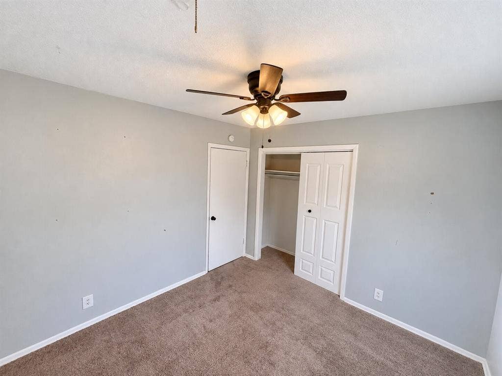 Interior room featuring neutral-tone carpeting, a multi-panel closet door, a solid-panel door, and a ceiling-mounted light fixture with a central fan