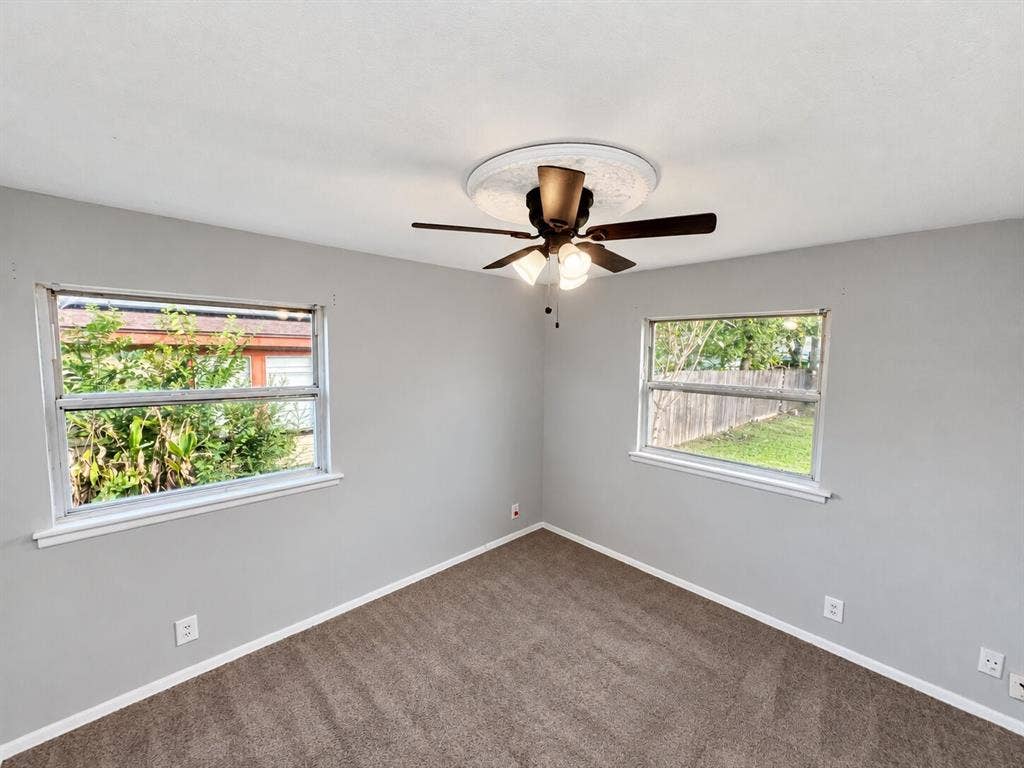 Neutral-toned interior featuring dual windows, carpeting, and a central ceiling fan with a light fixture and decorative medallion
