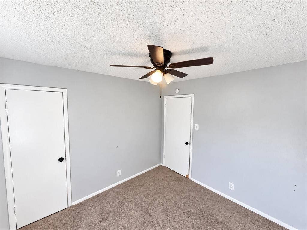 Neutral-toned interior walls, textured ceiling, carpeted flooring, two interior doors, and a ceiling-mounted light fixture with a three-blade fan