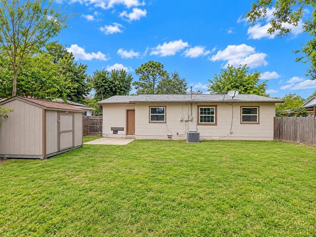 Rear exterior featuring a spacious grass lawn, concrete patio, detached storage shed, and wood-fence perimeter