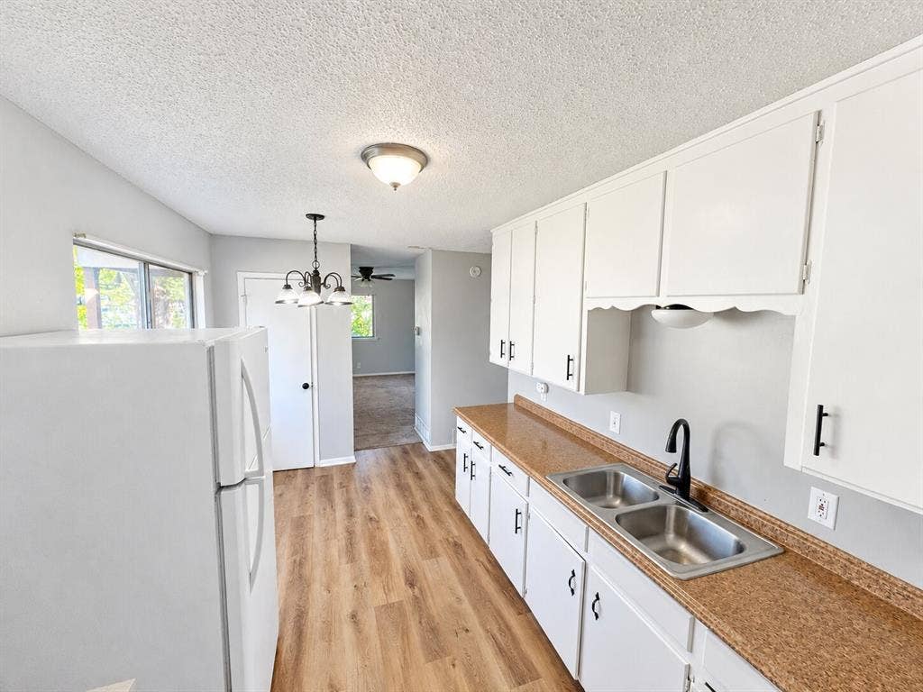 Kitchen featuring wood-finish flooring, white cabinetry with matte black hardware, dual-basin stainless steel sink with a high-arch faucet, and laminate countertops