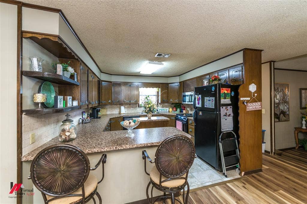 Kitchen featuring wood cabinetry, integrated open shelving, speckled laminate countertops, peninsula with bar seating, and wood-finish flooring