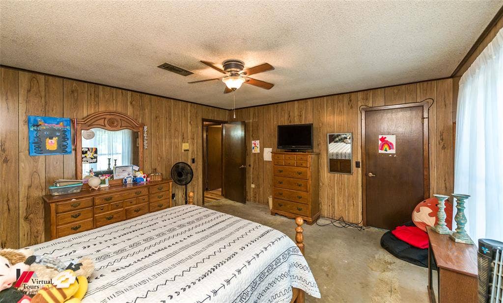 Interior room featuring wood-panel wall finish, textured ceiling, and a central ceiling fan with integrated lighting