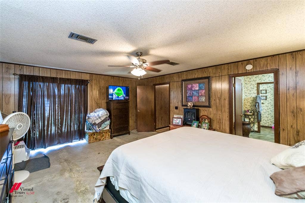 Wood-panelled wall treatments, ceiling-mounted paddle fan with integrated lighting, and sliding glass door with dark drapery
