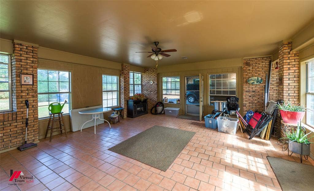 Enclosed patio featuring exposed brick columns, ceramic tile flooring, a ceiling fan with integrated lighting, and multiple windows