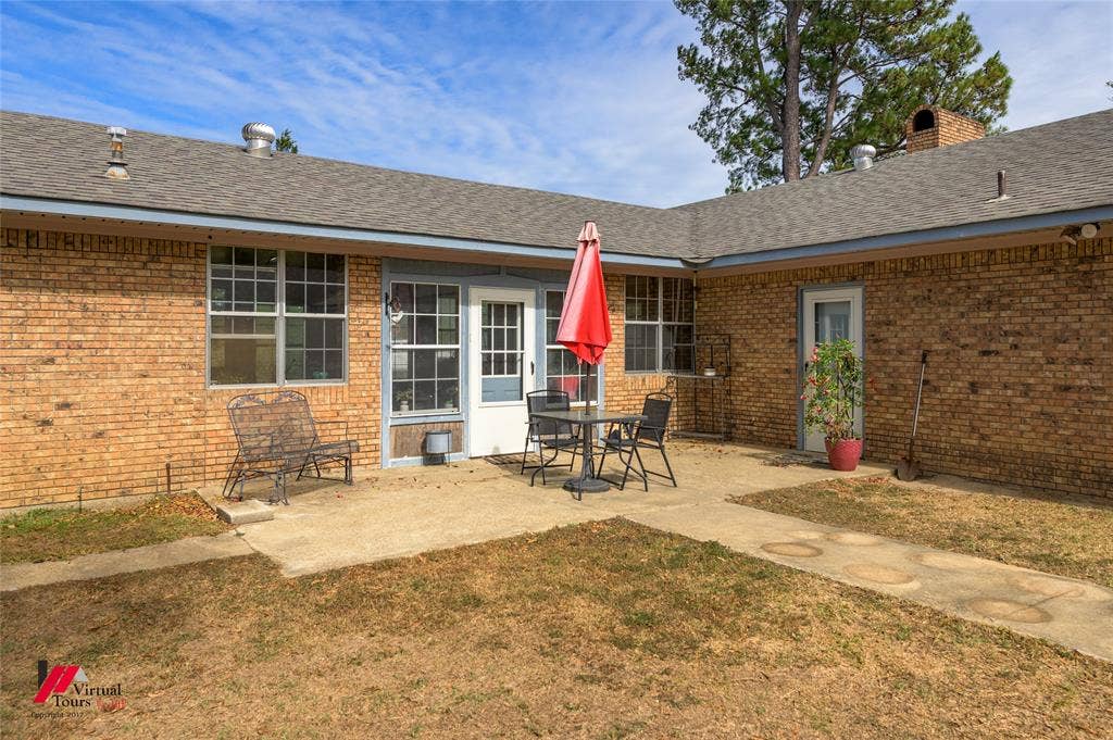 Brick exterior featuring a concrete patio, multi-pane windows, and a shingle roof
