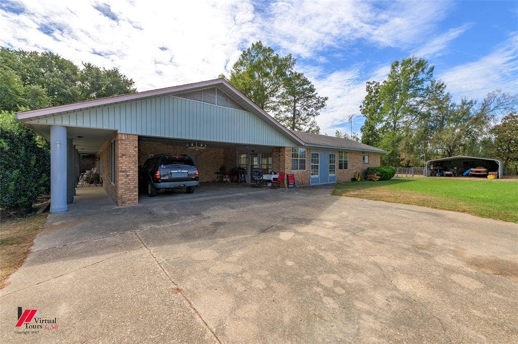 Exterior featuring a brick facade, expansive concrete driveway, covered parking area, and detached metal structure