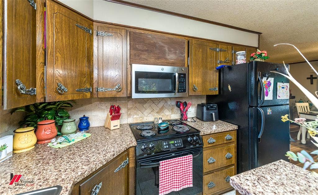 Kitchen featuring wood cabinetry with decorative metal hardware, stone-patterned countertops, a stone tile backsplash in a herringbone pattern, and built-in stainless steel microwave