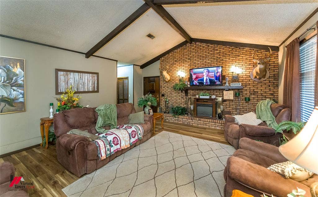 Vaulted ceiling featuring exposed structural beams, floor-to-ceiling brick hearth, and wood-finish flooring