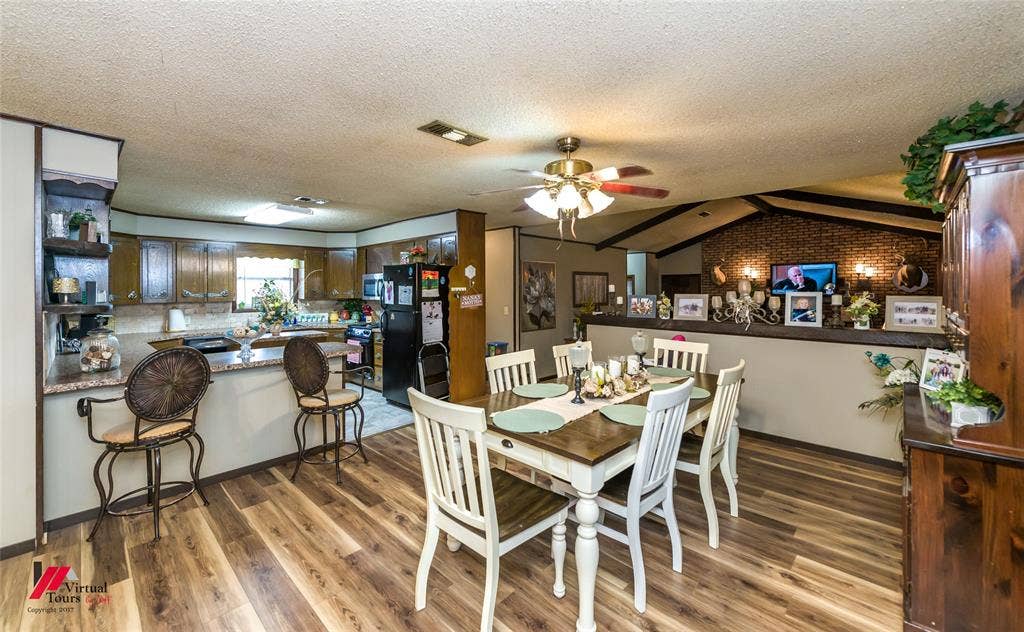 Open-concept dining area featuring wood-finish flooring, a brick accent wall, and a breakfast bar with stone-finish countertops