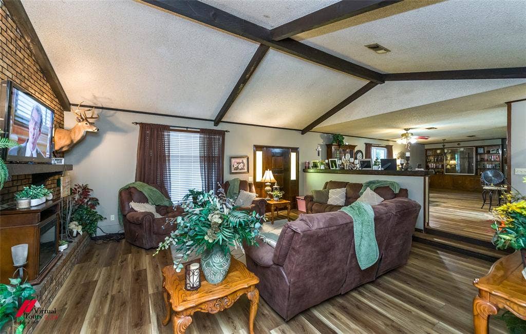 Vaulted ceiling with exposed decorative beams, floor-to-ceiling brick hearth, and wood-finish flooring