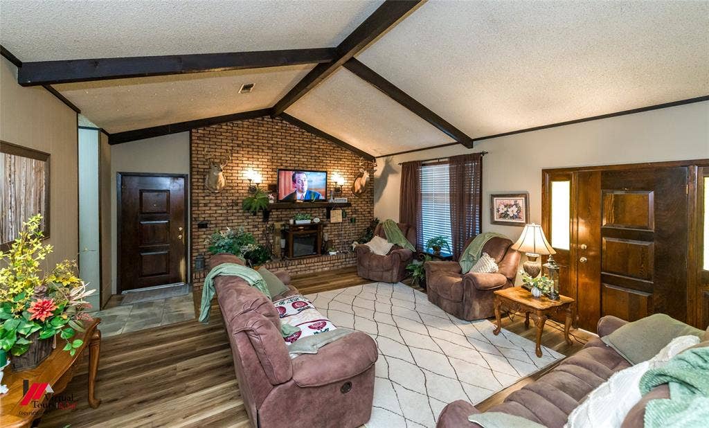 Vaulted ceilings with exposed beams, floor-to-ceiling brick accent wall, wood-finish flooring, and dark wood-paneled doors