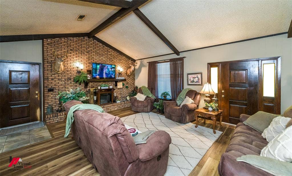 Vaulted ceiling with exposed decorative beams, full-height brick masonry fireplace, and wood-finish flooring