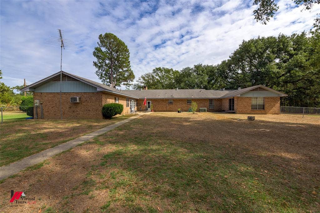 Single-story brick exterior featuring a multi-gabled roofline, concrete walkway, and expansive backyard with mature tree canopy