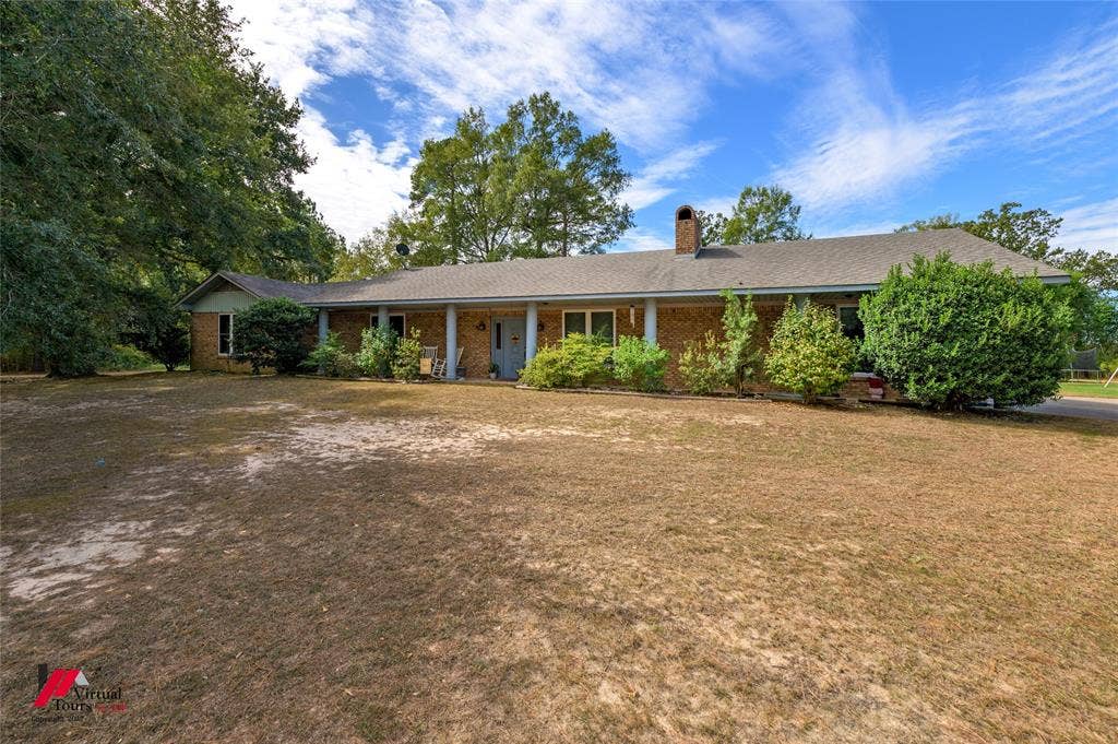Single-story ranch exterior featuring a brick facade, covered front porch with support columns, asphalt shingle roof, and a prominent brick chimney