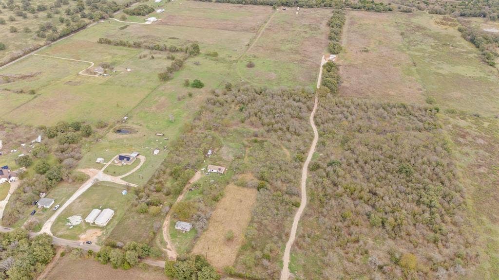870 Wagoner Road, Waco, TX 76705 Expansive rural acreage featuring cleared pastureland, dense clusters of mature trees, and existing unpaved trail access