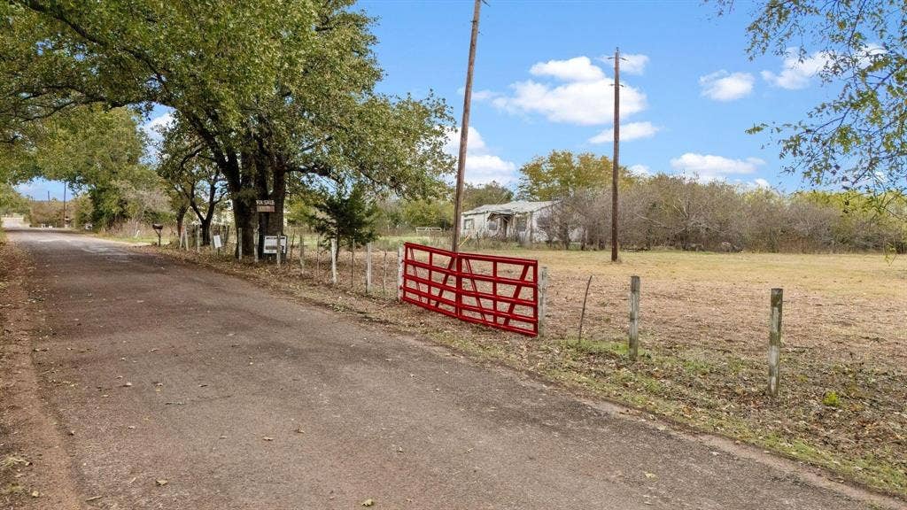 870 Wagoner Road, Waco, TX 76705 Expansive acreage featuring mature trees, perimeter wire fencing, and a red metal swing gate