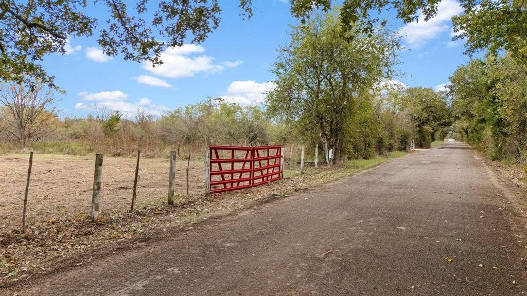 870 Wagoner Road, Waco, TX 76705 Expansive acreage featuring wire fencing, a metal gate, mature trees, and frontage on a paved road