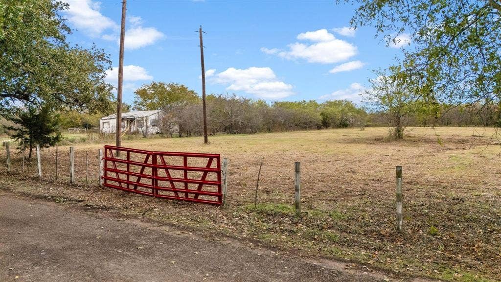 870 Wagoner Road, Waco, TX 76705 Expansive level lot featuring a red metal tube gate, wire perimeter fencing, and mature trees
