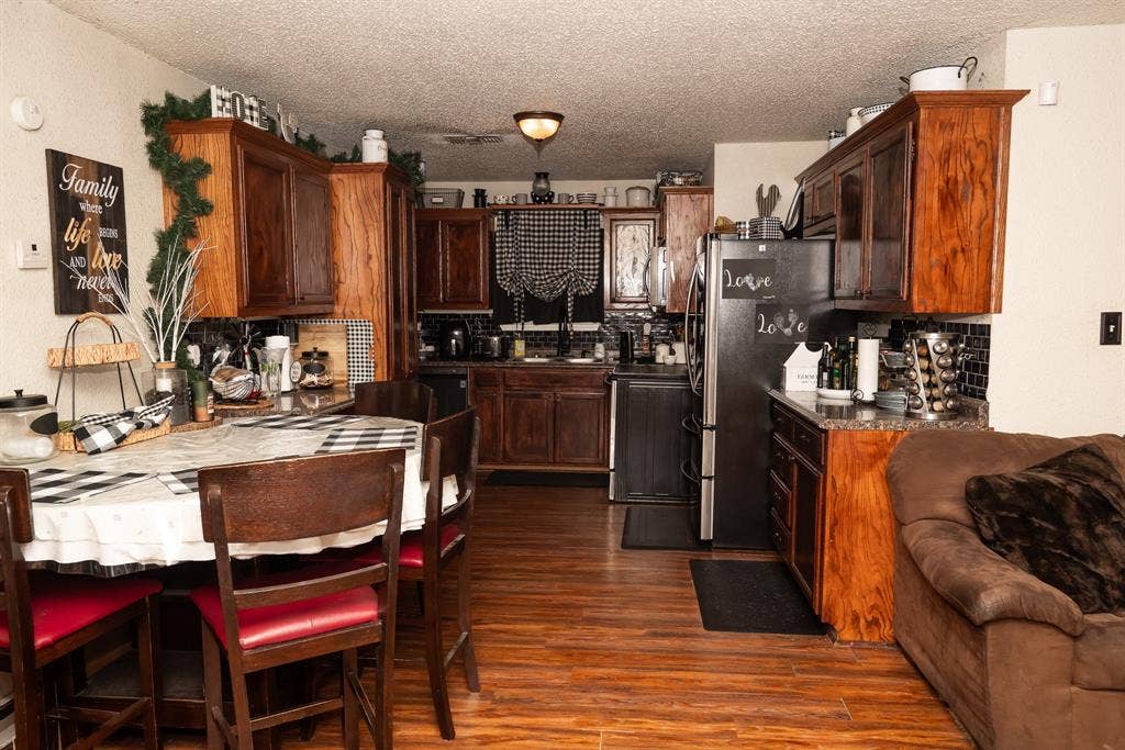 Kitchen featuring stained wood cabinetry, stone-finish countertops, subway tile backsplash, built-in stainless steel appliances, and wood-finish flooring