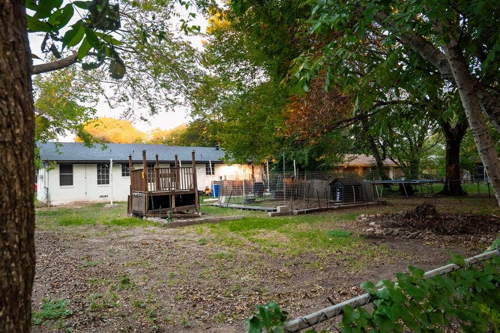 Expansive backyard featuring a raised wooden deck, wire-mesh fencing, mature trees, and a level lawn