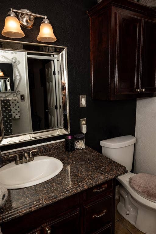 Dark-stained cabinetry, stone-surface countertop with an integrated basin, framed wall mirror, dual-shade vanity lighting, and built-in upper storage cabinet