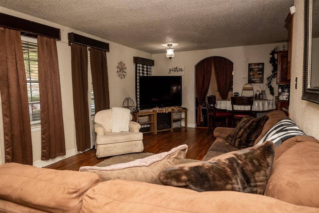 Living area featuring wood-finish flooring, textured ceilings, and a prominent arched entryway