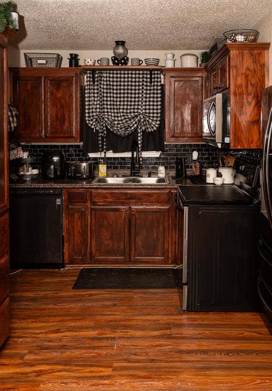Kitchen featuring wood-finish cabinetry, dark tile backsplash, wood-finish flooring, integrated appliances, and a dual-basin sink with a high-arch faucet