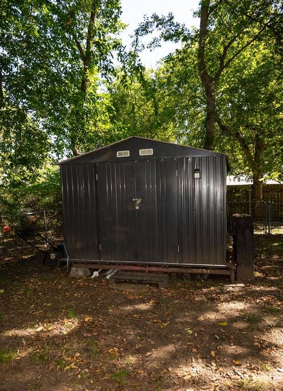 Dark-toned metal storage structure featuring dual doors and dual gable vents, set upon an elevated steel frame foundation