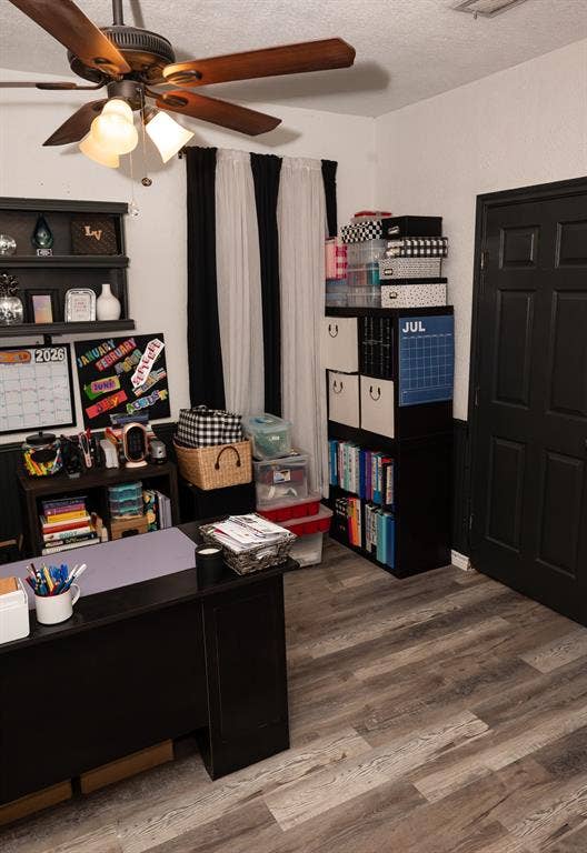 Wood-finish flooring, ceiling fan with integrated lighting, and a six-panel door with a dark finish