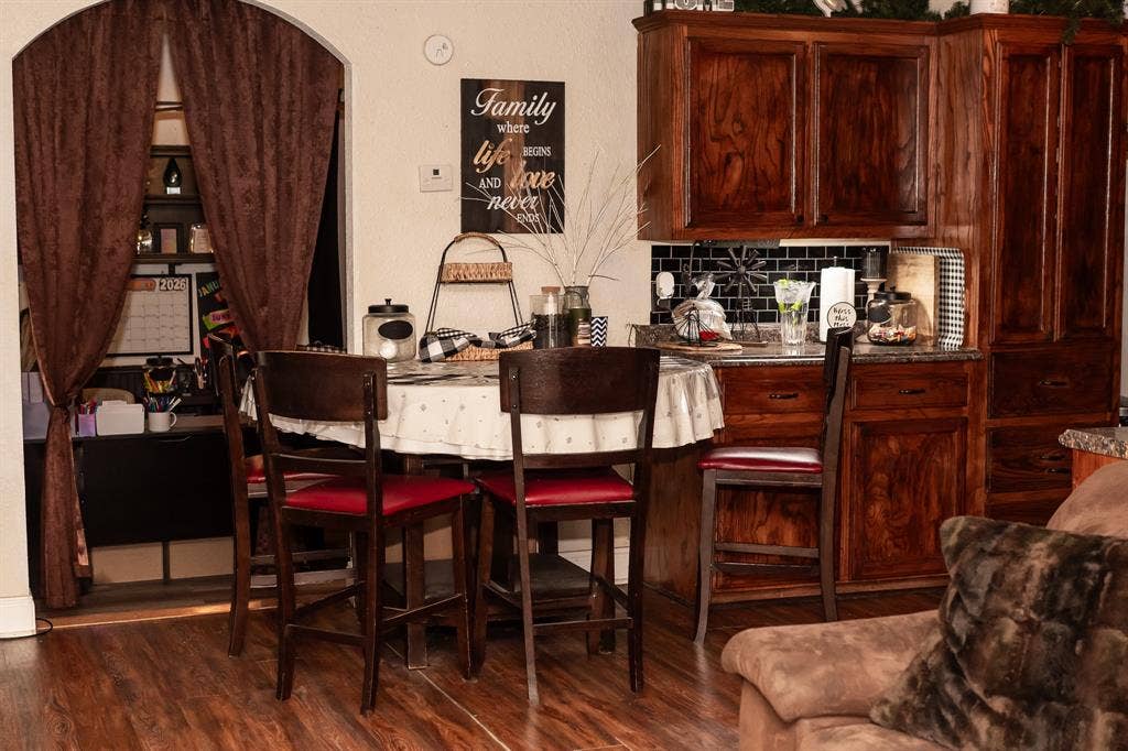 Stained wood cabinetry, black subway tile backsplash, arched doorway, and wood-finish flooring