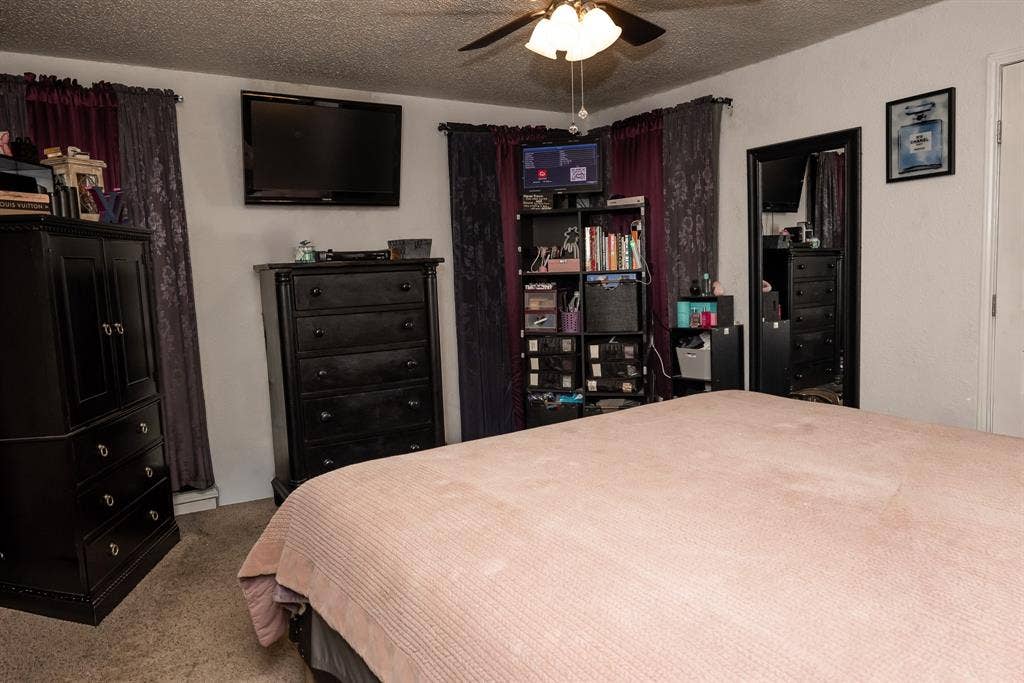 Bedroom featuring neutral-toned carpeting, a multi-blade ceiling fan with integrated lighting, and a solid-core entry door