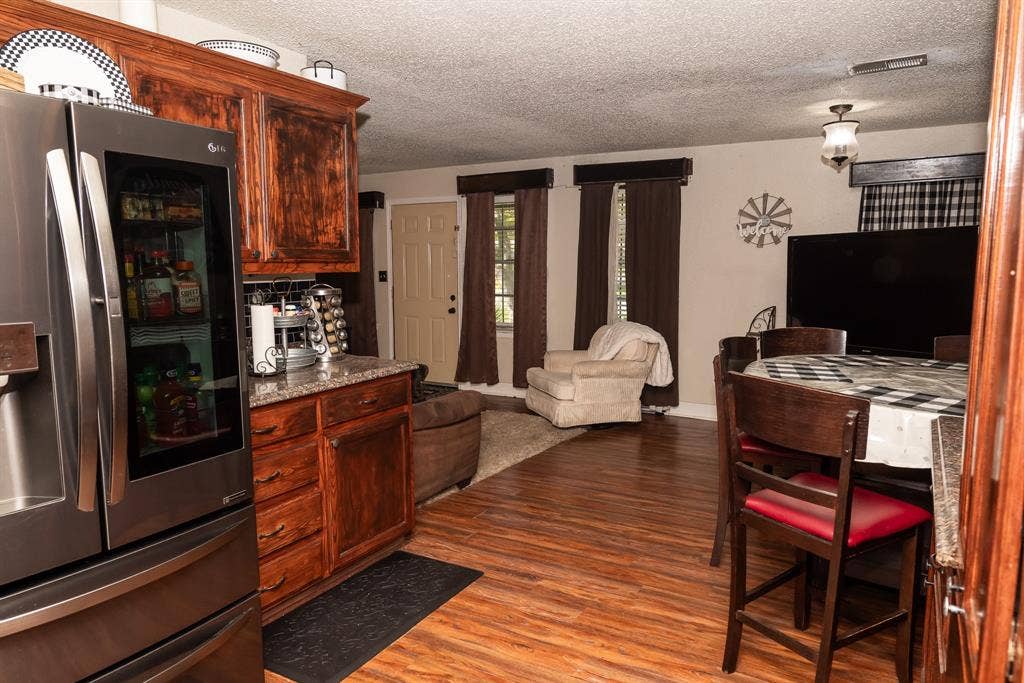 Stained wood cabinetry, speckled stone-finish countertops, stainless steel refrigerator, and wood-finish flooring