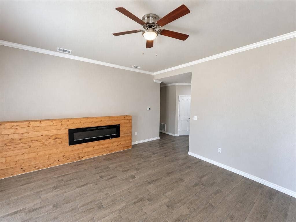 1306 Campbelton Drive, Temple, TX 76504 Interior space featuring wood-finish flooring, a wood-paneled accent wall with a built-in linear fireplace, a multi-blade ceiling fan with integrated lighting, and crown molding