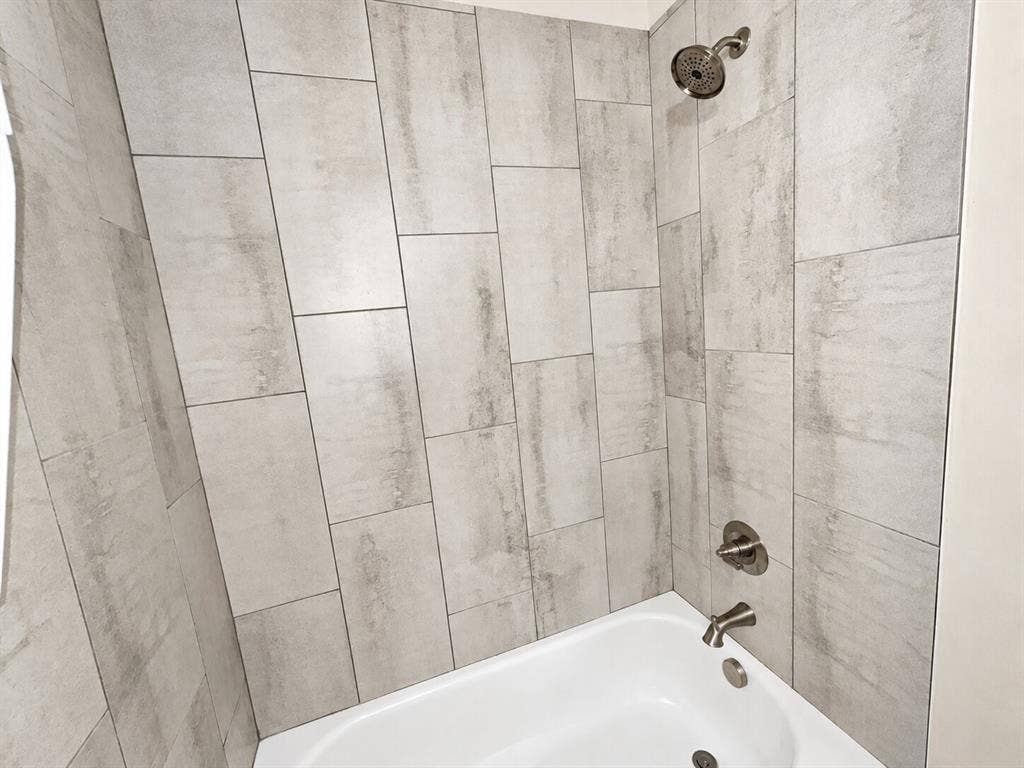 1306 Campbelton Drive, Temple, TX 76504 Shower and bathtub combination featuring large-format stone-finish wall tiling in a vertical offset pattern, stainless steel fixtures, and a wall-mounted shower head